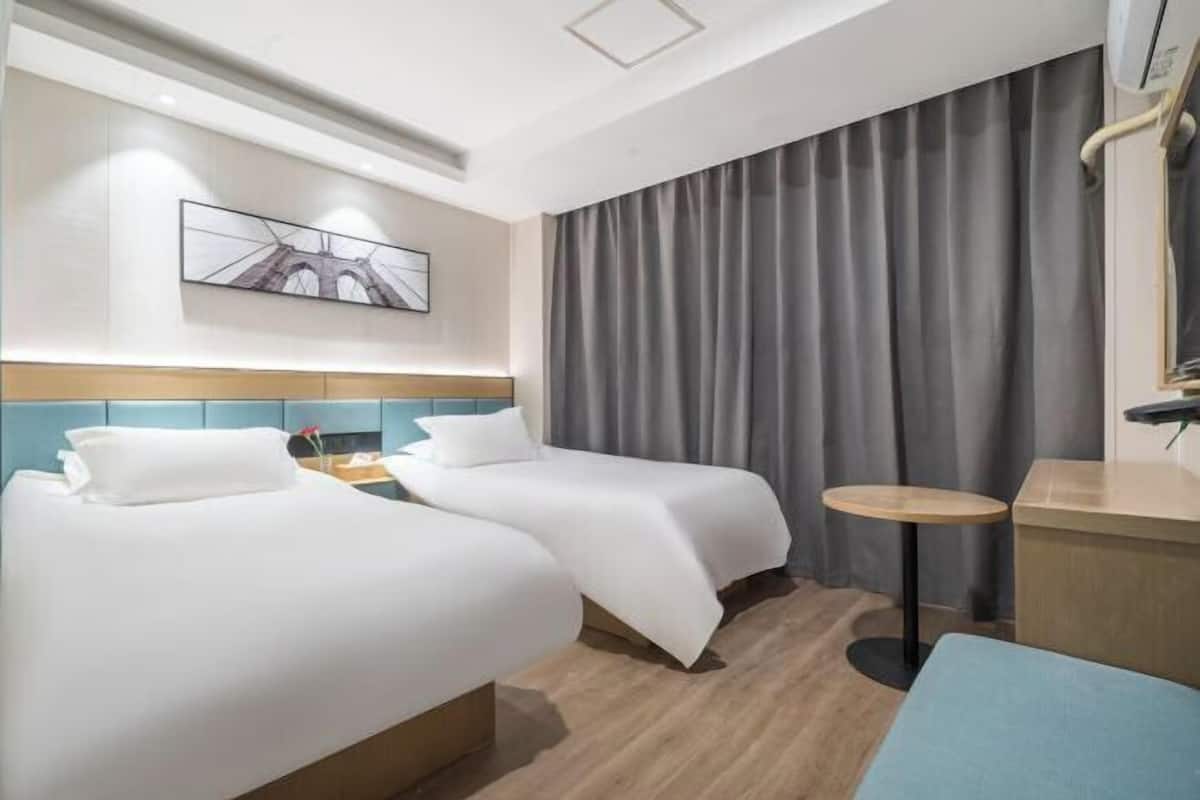 Ein Hotelzimmer mit zwei Betten, einem runden Tisch, einem Bild an der Wand und einem großen Fenster mit Vorhängen.