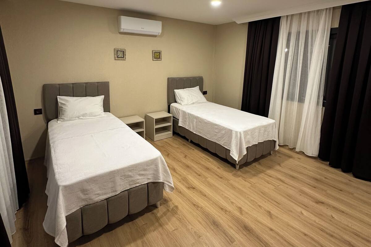 Habitación de hotel con dos camas, piso de madera, aire acondicionado y ventana con cortinas.