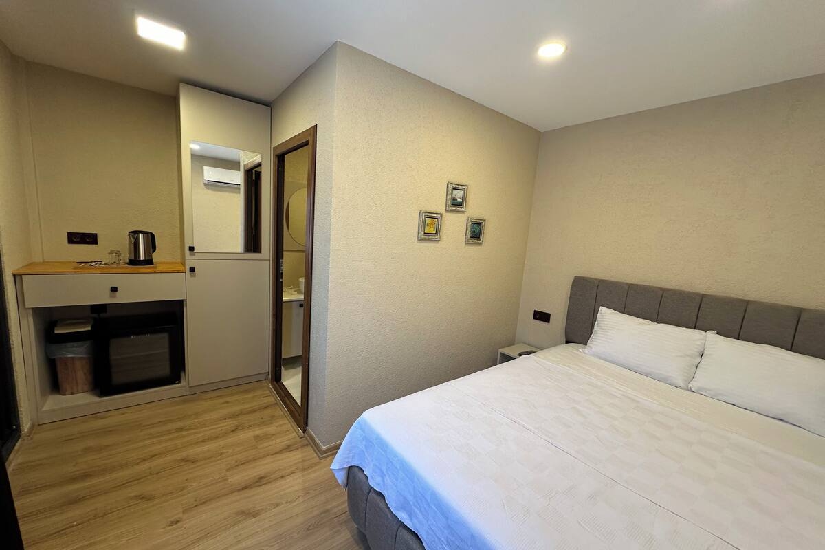 Una habitación de hotel con una cama, un escritorio pequeño con un hervidor, un espejo y un cubo de basura.