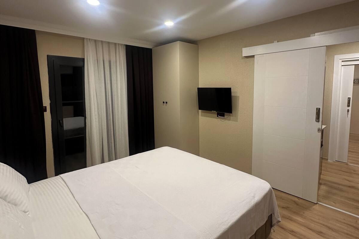 Una habitación de hotel con una cama grande, un televisor de pantalla plana montado en la pared, una puerta con picaporte y una lámpara en el techo.