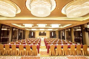 A banquet hall with rows of tables and chairs, large chandeliers, and a carpeted floor.