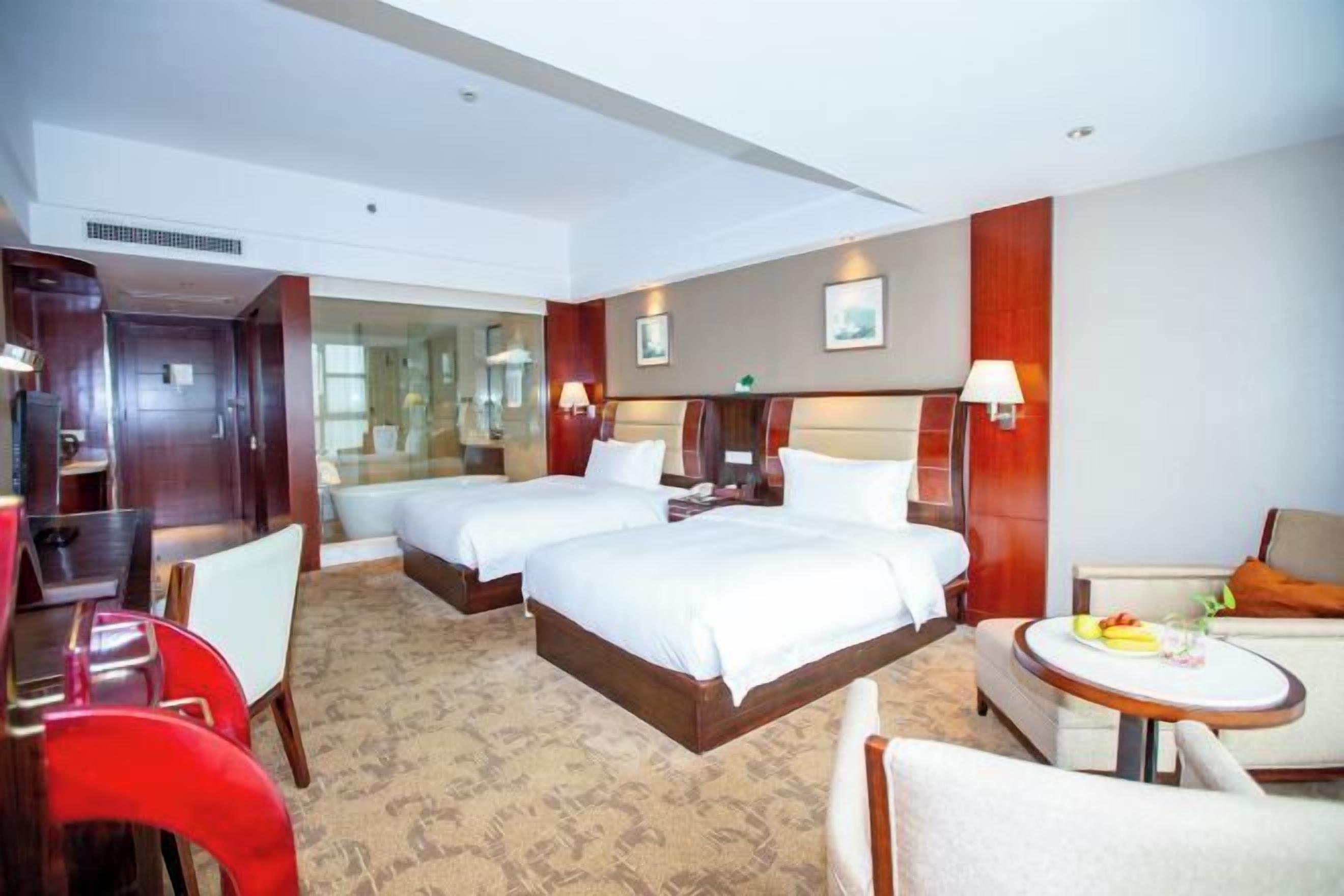 A hotel room with two beds, a desk, a chair, a sofa, and a small round table with a fruit plate.