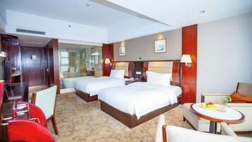 A hotel room with two beds, a desk, a chair, a sofa, and a small round table with a fruit plate.