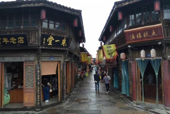 Une rue étroite bordée de bâtiments traditionnels en bois, de boutiques et d’lanternes suspendues.