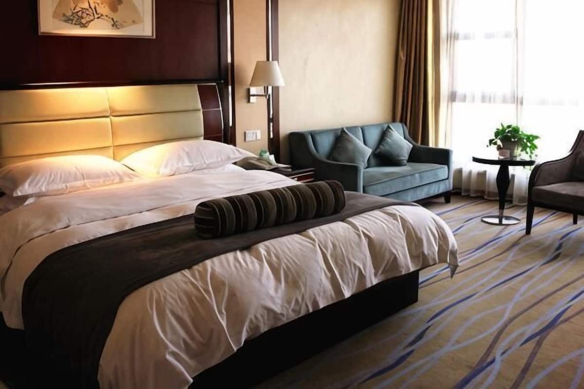 Une chambre d’hôtel avec un grand lit, un canapé, une petite table et une plante en pot.