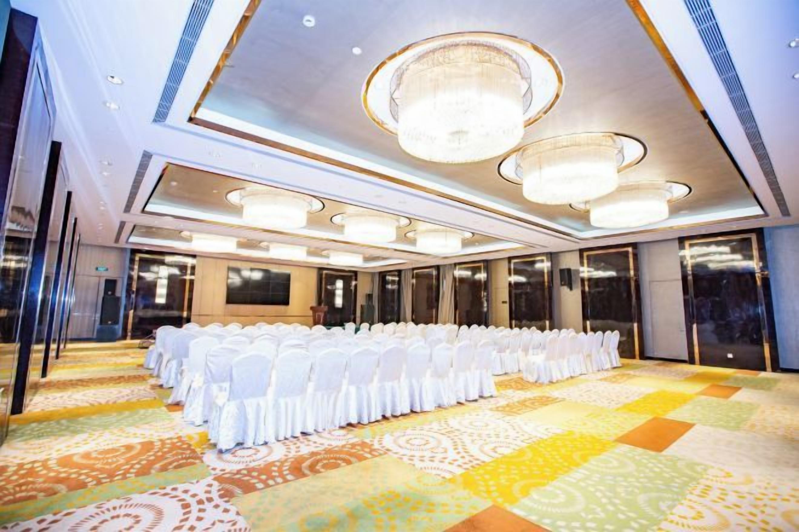 A conference room with rows of white chairs, a patterned carpet, and a chandelier.