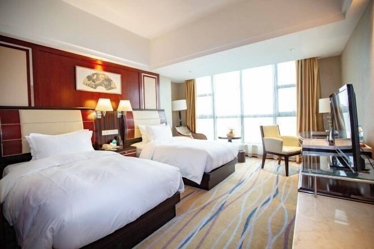 Une chambre d’hôtel avec deux lits, un bureau, une télévision et de grandes fenêtres.