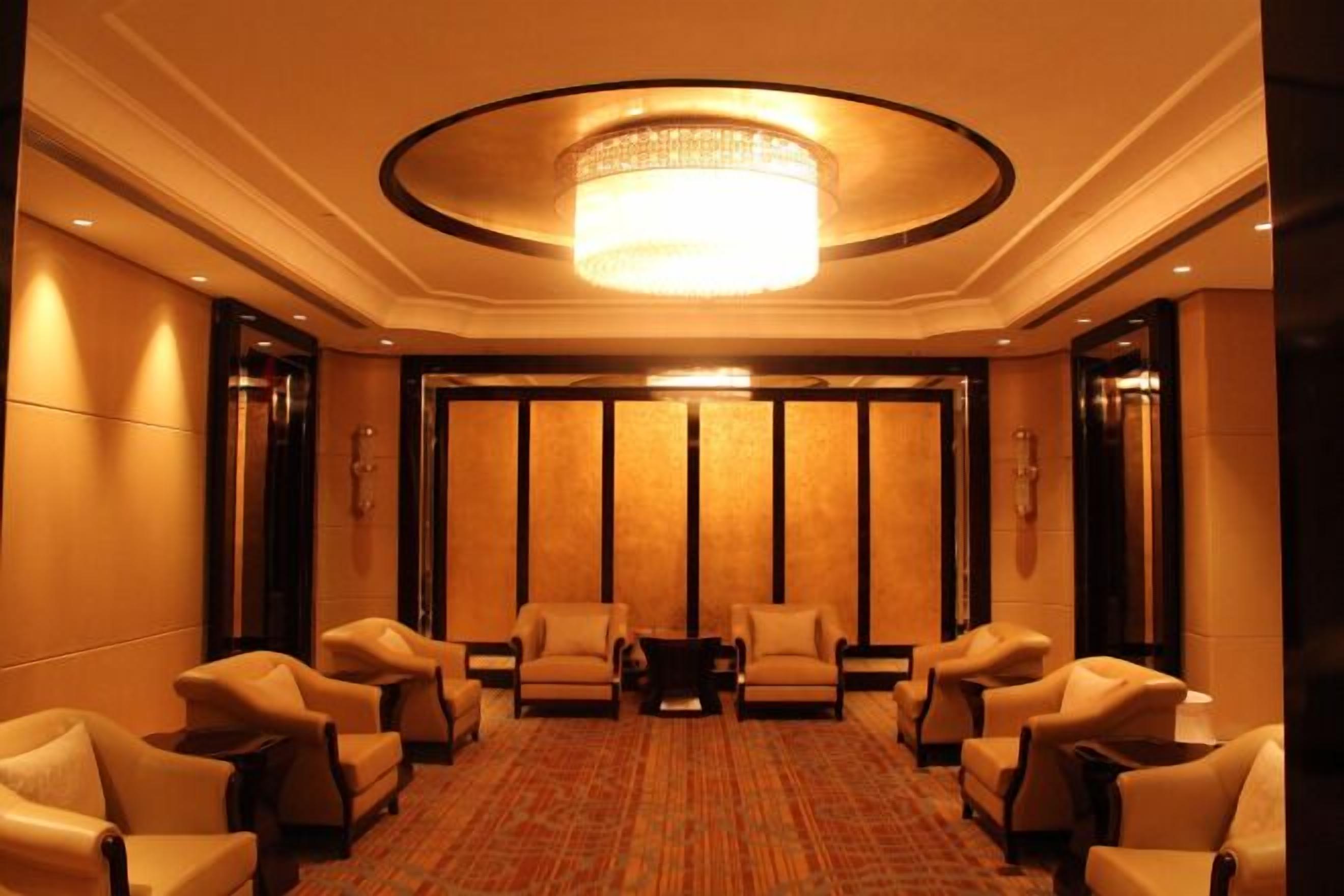 A hotel lobby with a central chandelier, seating area with chairs, and a patterned carpet.