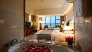 Een hotelkamer met een groot bad vol rozenblaadjes, een bed met uitzicht op de stad en een bureau met een lamp.