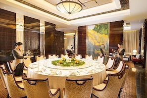 A formal dining room with a round table, chairs, and a large painting on the wall.