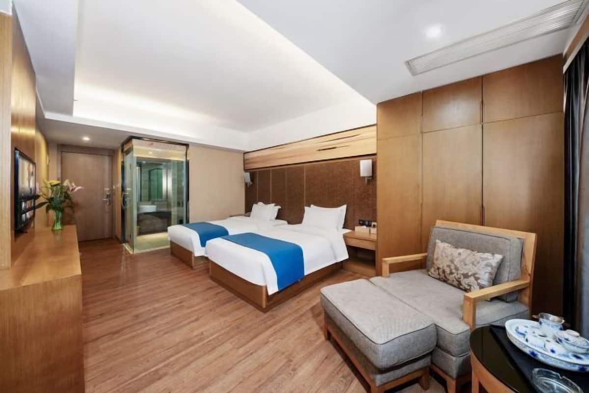 A hotel room with two beds, a sofa, a small table, and a glass door leading to a bathroom.