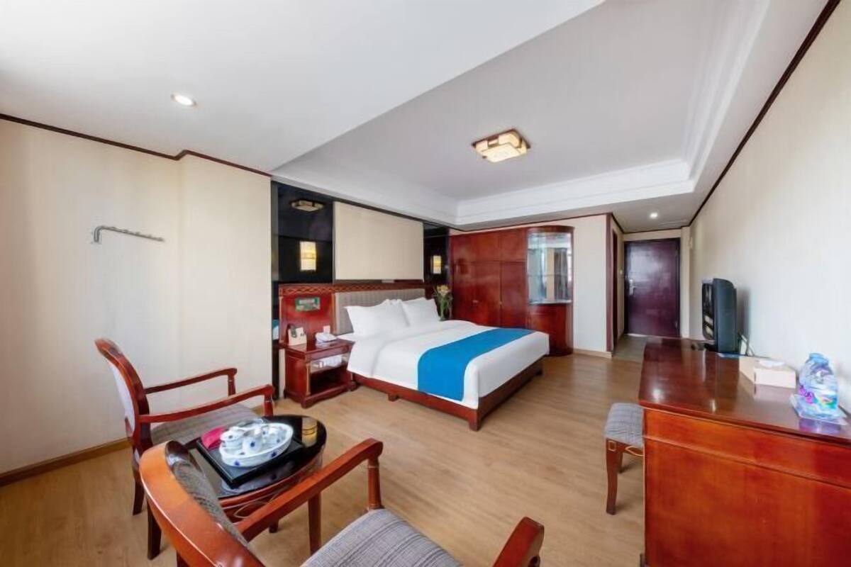 A hotel room with a bed, desk, chair, and a small table with a tray.