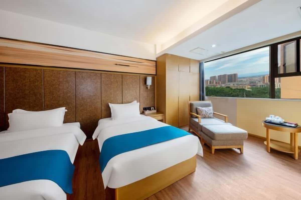 A hotel room with two beds, a sofa, a small table, and a large window offering a city view.