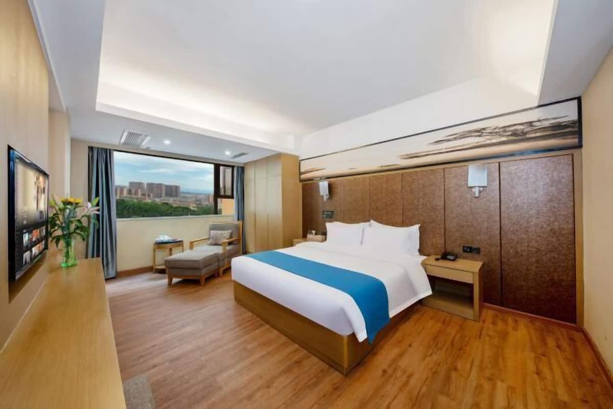 A hotel room with a large bed, a desk, a chair, a nightstand, and a view of the city.