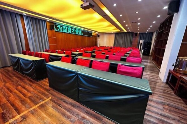 A conference room with rows of tables and chairs, wooden flooring, and a large screen on the wall. - Jinheyuan International Hotel Guide (Guide)