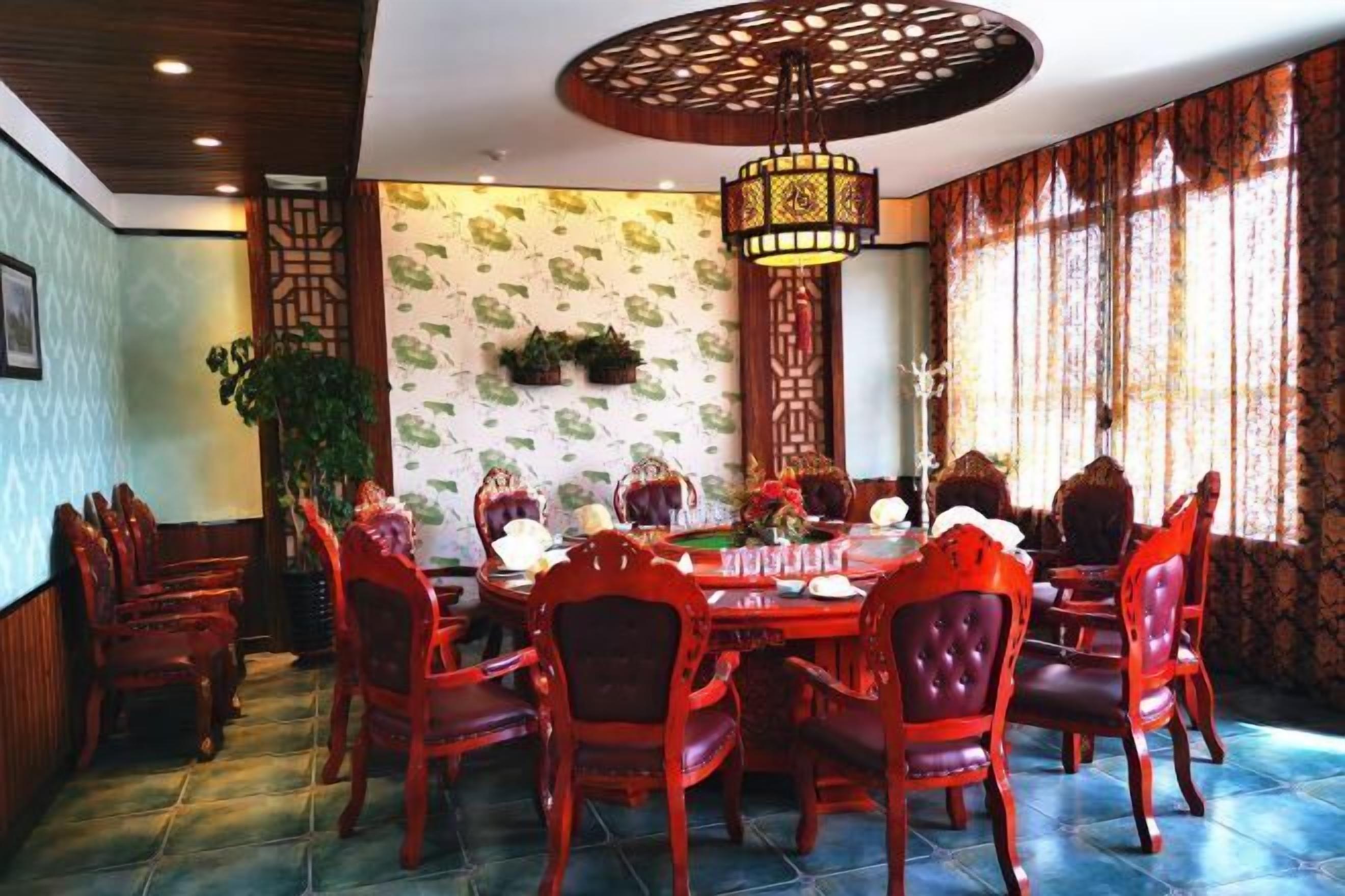 Un comedor con una mesa redonda, sillas rojas, una lámpara colgante decorativa y papel tapiz estampado.