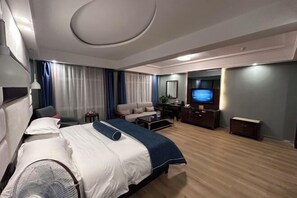 A hotel room with a bed, a TV, a sofa, a desk, and a fan. - Jinheyuan International Hotel Guide (Guide)