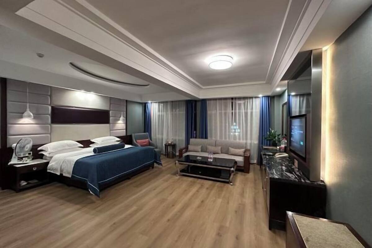 A hotel room with a bed, a sofa, a coffee table, a TV, and a desk with a lamp.