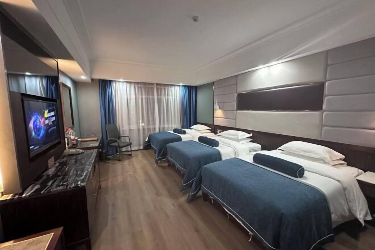 A hotel room with a TV, three beds, a desk, and a chair.