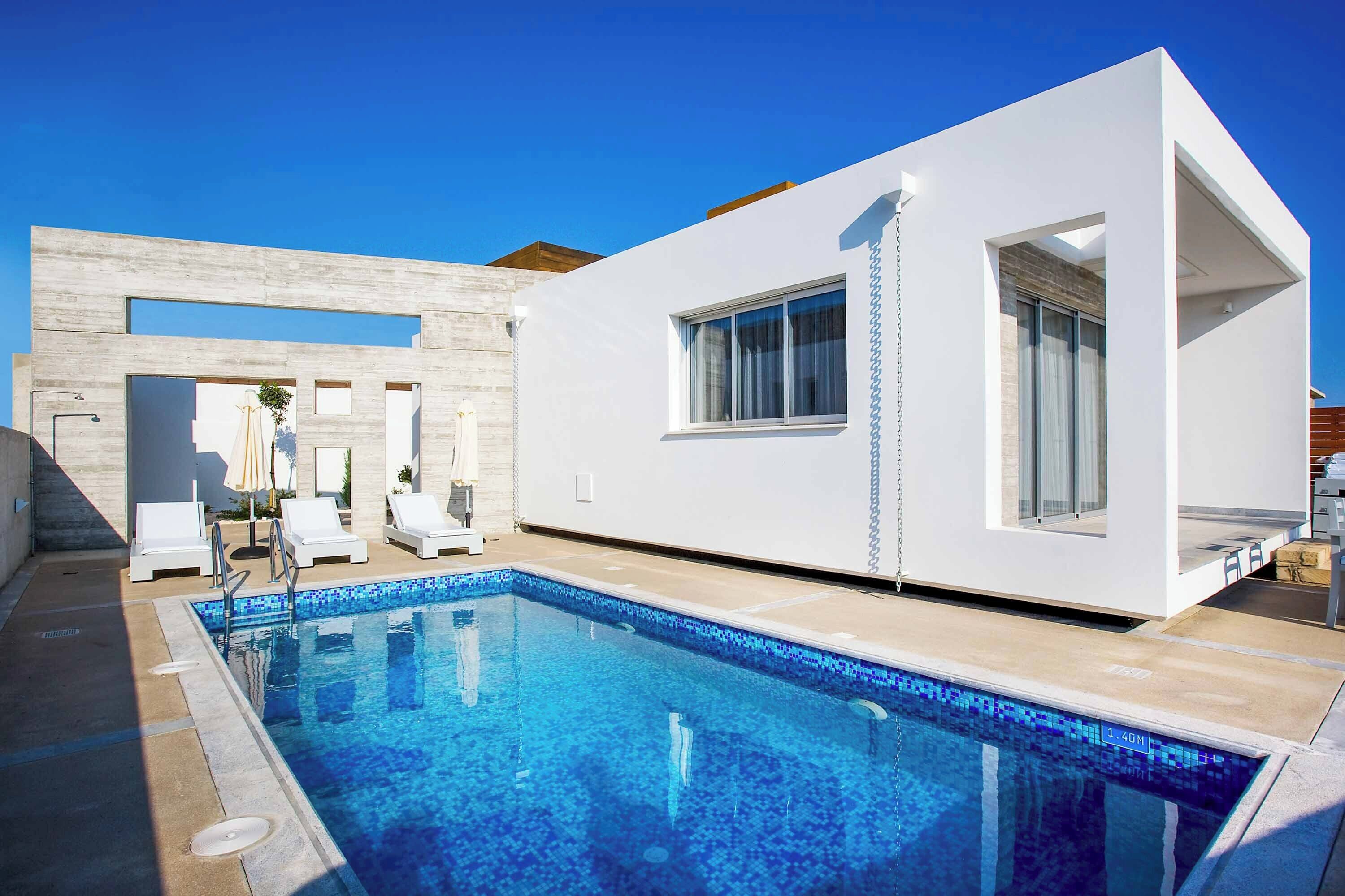 Un espace moderne aménagé autour d’une piscine, avec une eau d’un bleu limpide, des murs blancs et un design minimaliste.