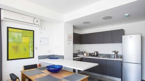 A modern kitchen with grey cabinets, a stainless steel refrigerator, and a dining area with a wooden table and black chairs. - Villa Cerulean Paphos (Paphos)