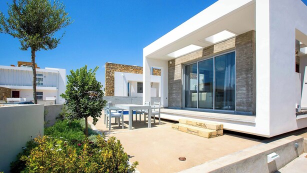 A modern house with a patio, a dining area, and a large window. - Villa Cerulean Paphos (Paphos)