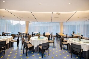 Ett konferensrum på ett hotell med runda bord, stolar och ett stort fönster med gardiner.