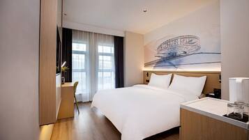 A modern hotel room with a large bed, a desk, and a large window.