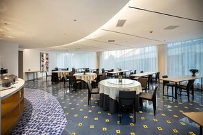 A modern dining area with round tables and chairs, a buffet counter, and large windows providing natural light. - Sangel Hotel(Zhengzhou Agricultural Road Store) (Zhengzhou)