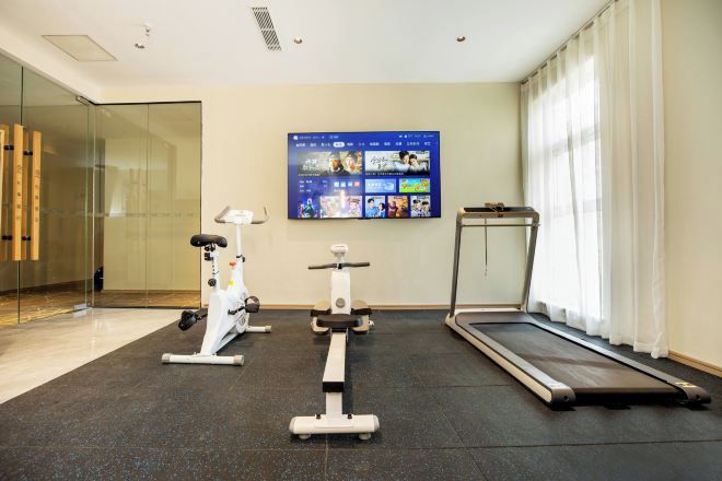 A modern gym with cardio equipment, a wall-mounted TV, and a window with curtains.