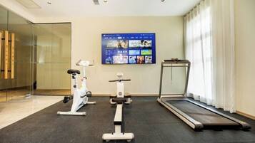 A modern gym with cardio equipment, a wall-mounted TV, and a window with curtains.