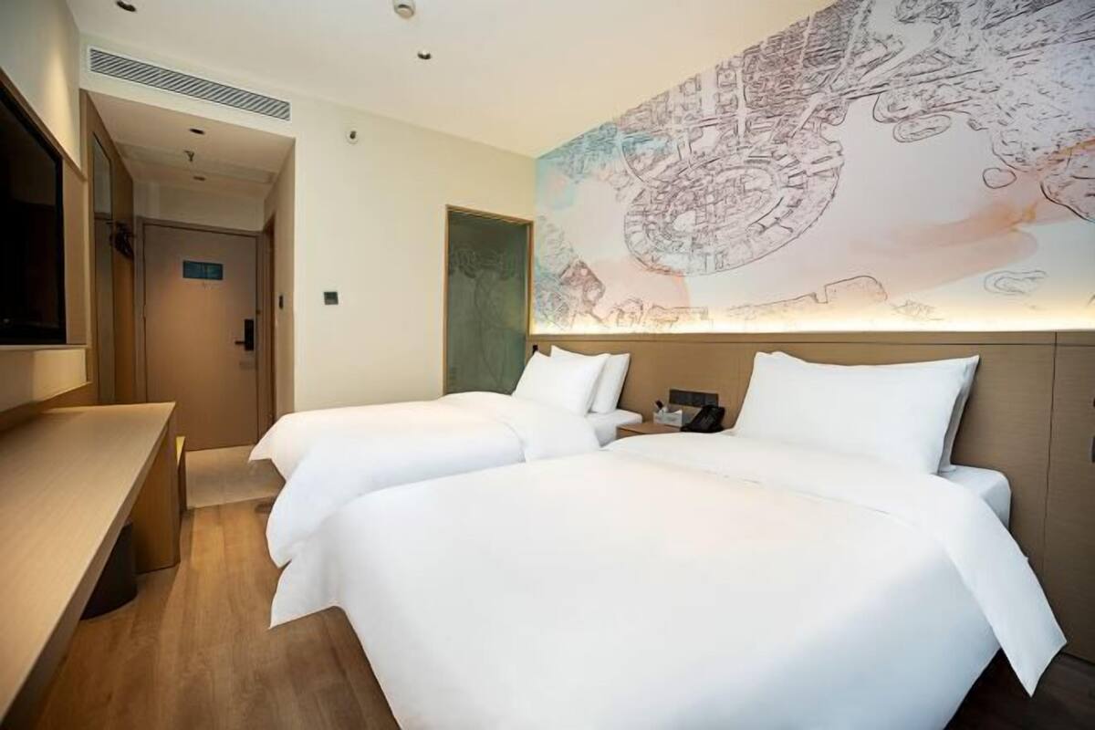 Habitación de hotel con dos camas, un escritorio y un mural grande con un mapa en la pared.