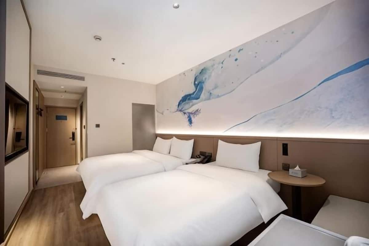 Habitación de hotel con dos camas, una mesa redonda y un cuadro abstracto grande en la pared.