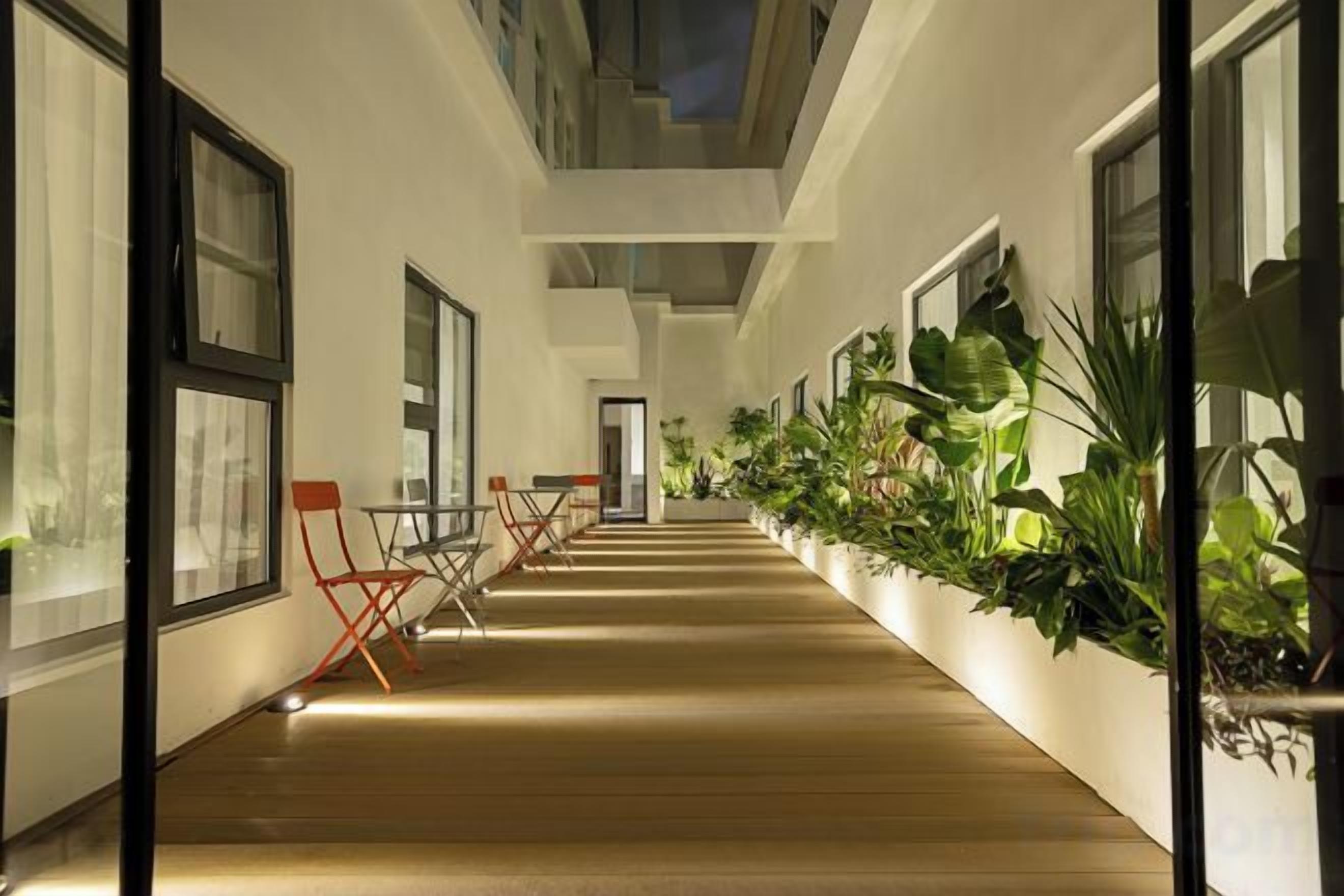 A corridor with wooden flooring, potted plants, and seating areas.
