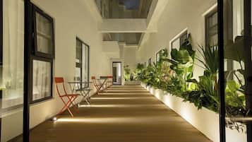 A corridor with wooden flooring, potted plants, and seating areas.