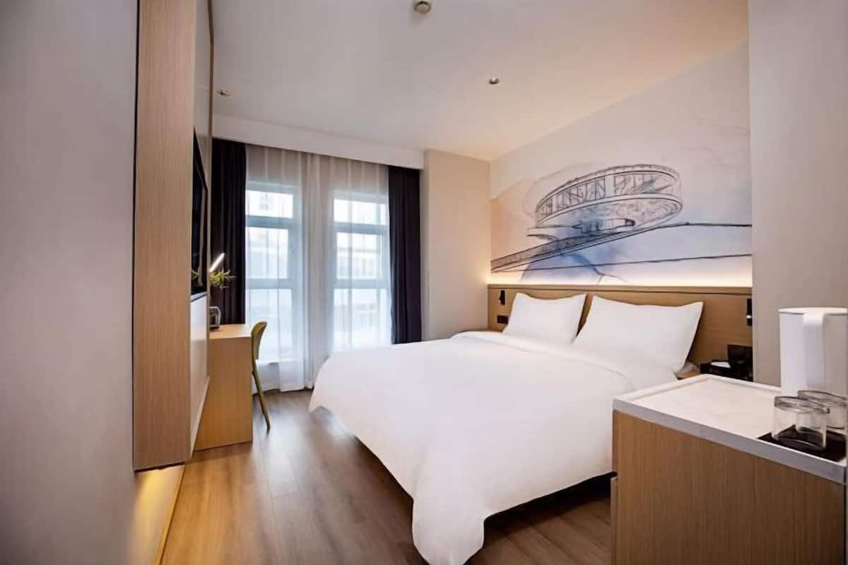 Una habitación de hotel moderna con una cama grande, un escritorio y una obra de arte colgada en la pared.