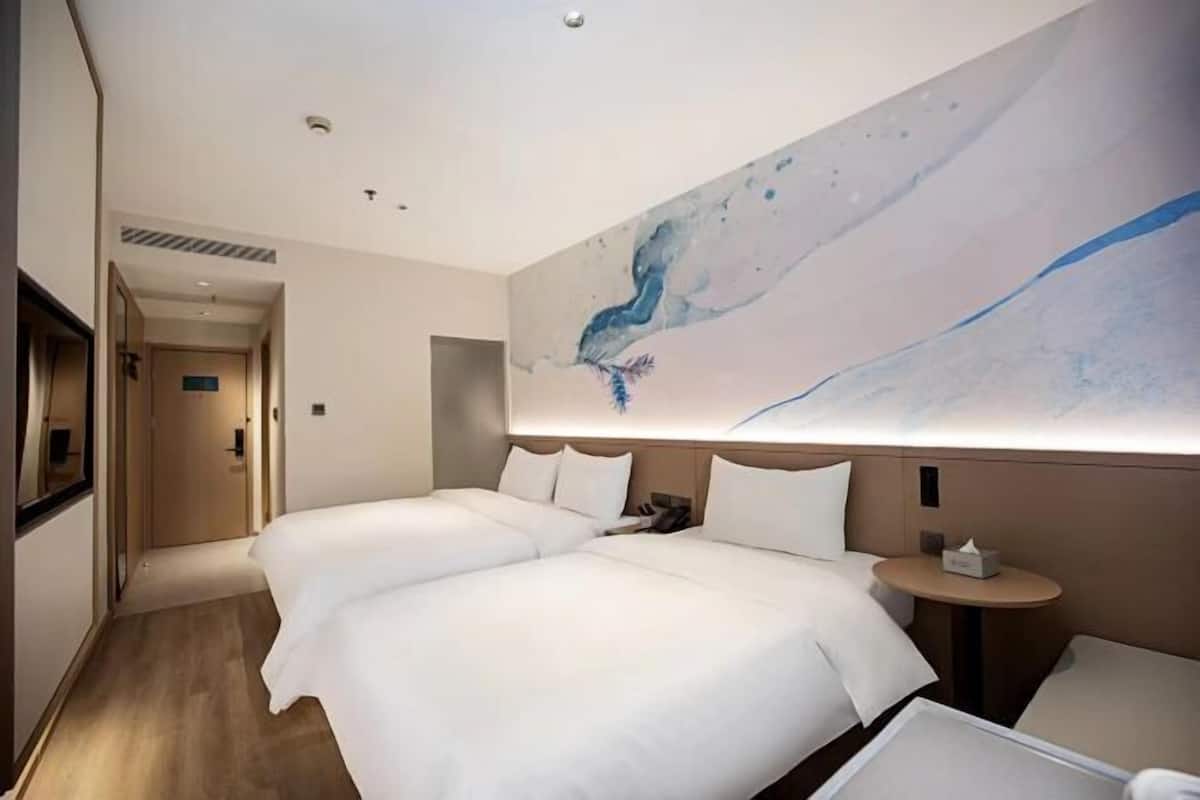 Habitación de hotel con dos camas, una mesa redonda y un cuadro abstracto grande en la pared.