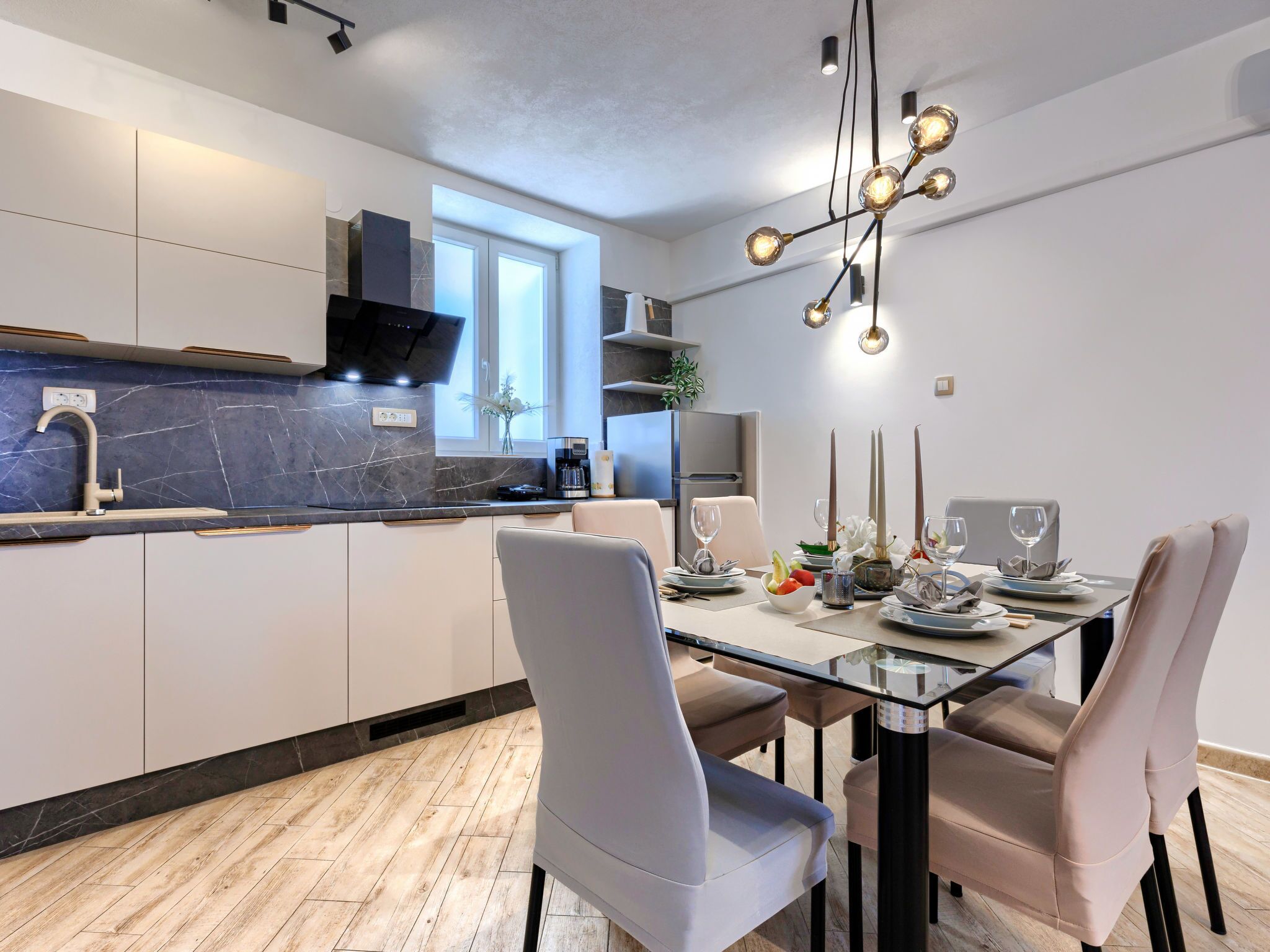 A modern kitchen with a built-in island, white cabinetry, and a glass dining table with chairs.