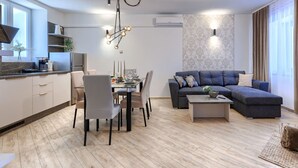 Una sala de estar moderna con un sofá gris, una mesa de comedor con sillas, una mesa de centro y una cocina con estufa y armarios.
