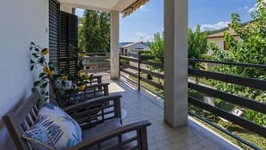 Un balcón con vistas a un jardín y una casa. Hay una mesa y un banco.