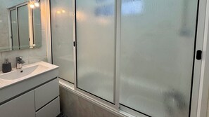 A bathroom with a white sink, a mirror, and frosted glass shower doors.