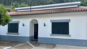 A building with a white facade, a tiled roof, and two windows with shutters.