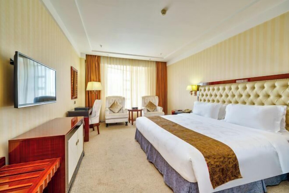 A hotel room with a bed, a desk, a chair, a television, and a window with curtains.