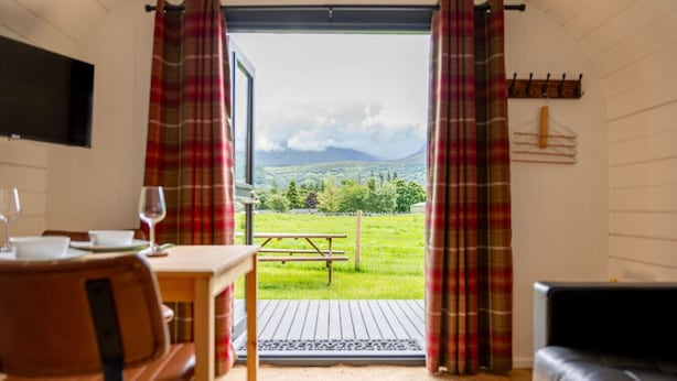 A room with a table and chairs, a bench outside, and a view of a grassy field and mountains. - Aonach Mor Pod near Fort William (Caol)