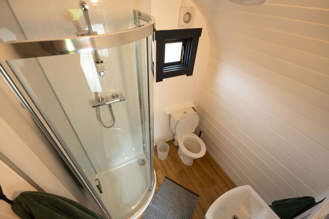 A compact bathroom with a glass-enclosed shower, a toilet, and a small window.
