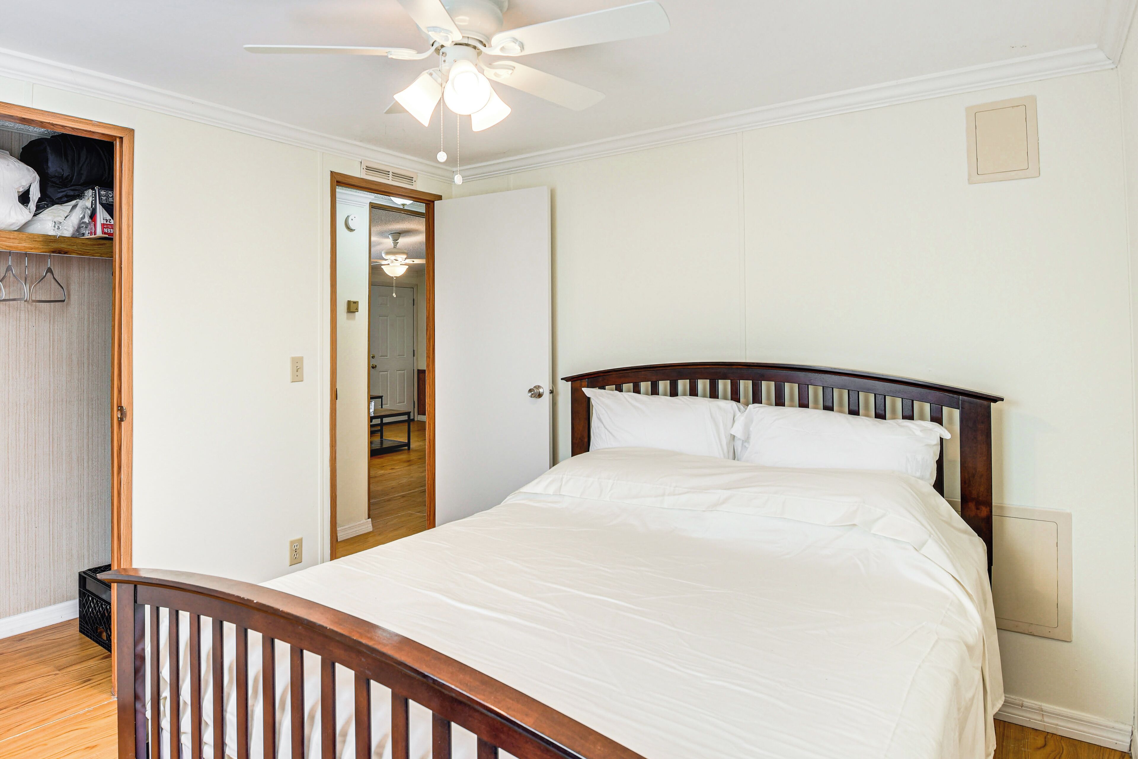A bedroom with a wooden bed frame, white bedding, a ceiling fan, and a walk-in closet.