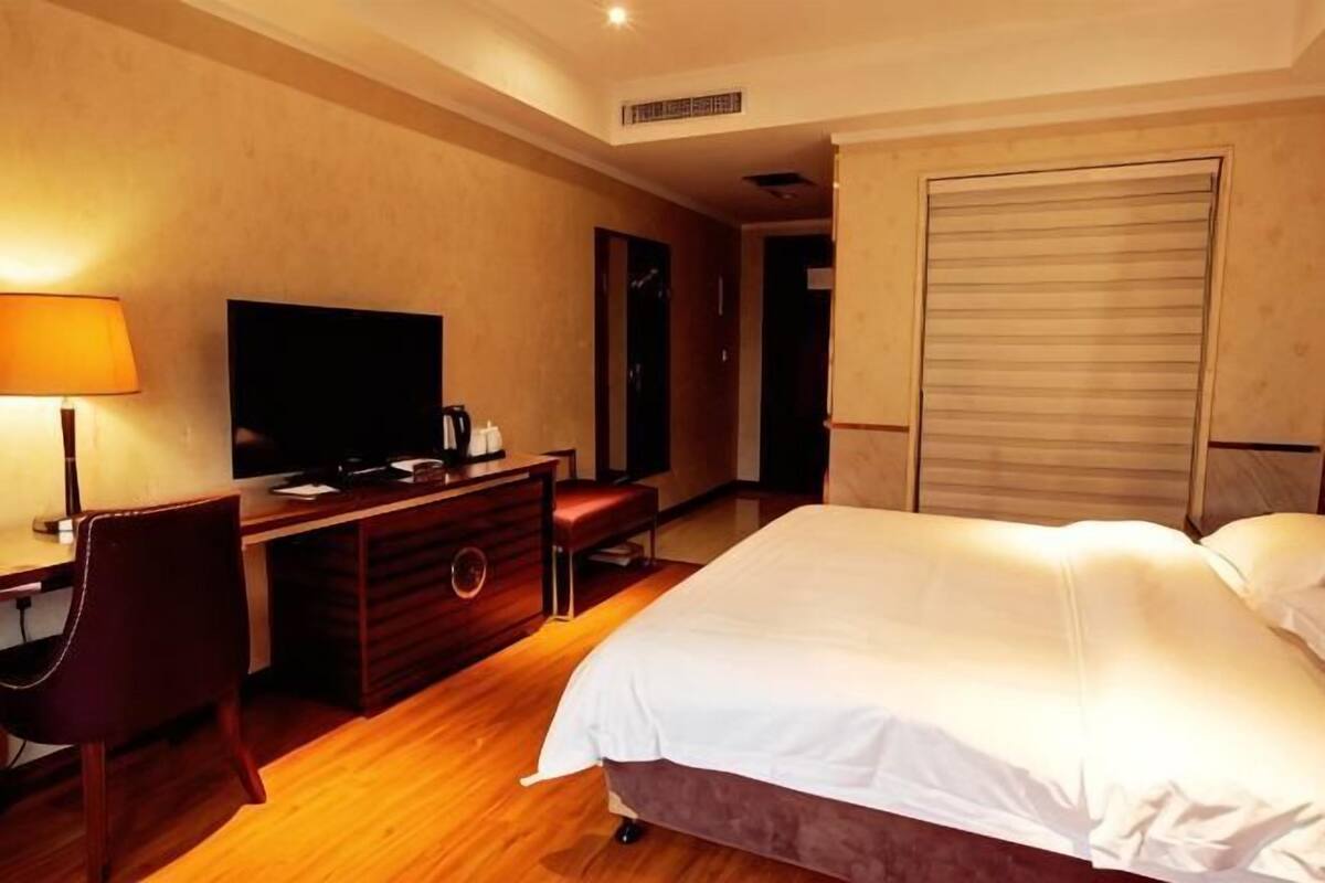 A hotel room with a bed, a desk with a TV, a chair, and a wardrobe.