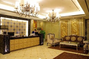 A hotel reception area with a reception desk, a receptionist, a sofa, and a chandelier. - Sunshine Business Hotel (Zhengzhou)