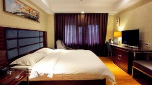 Habitación de hotel con una cama grande, un escritorio con televisor, una silla y un cuadro en la pared.