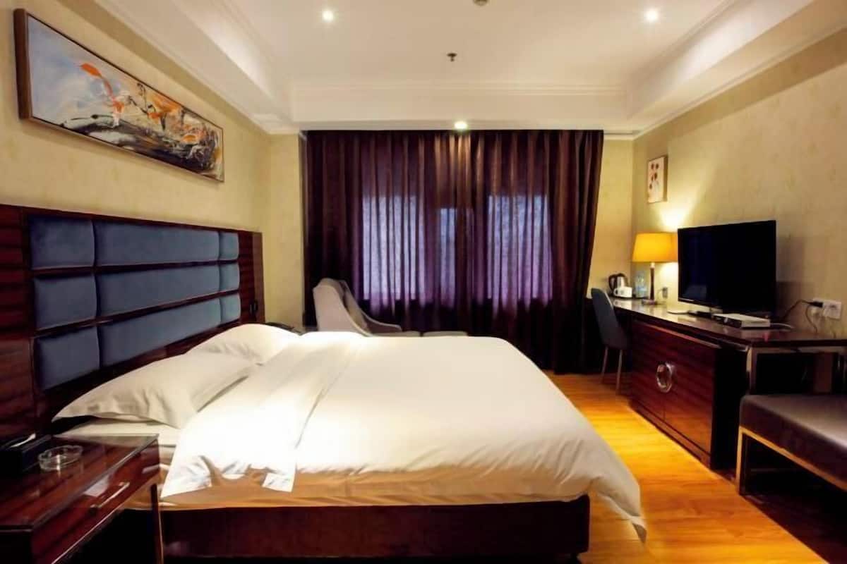 A hotel room with a large bed, a desk with a TV, a chair, and a painting on the wall.